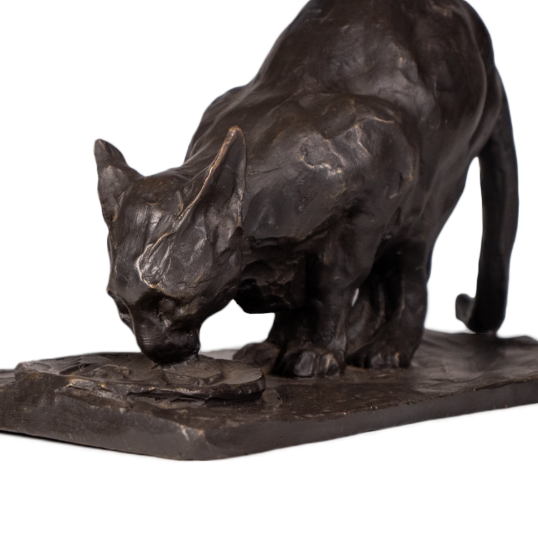 Detalle del gato de bronce bebiendo: cabeza de orejas puntiagudas junto al platillo, modelado a planos y pátina oscura